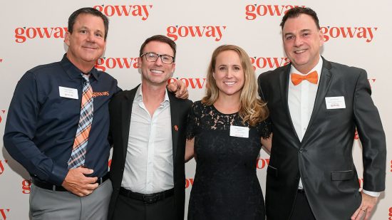 Four people pose in front of a display advertising Goway.