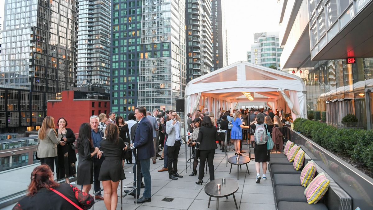 A group of people having a business party on a rooftop surrounded by condos.