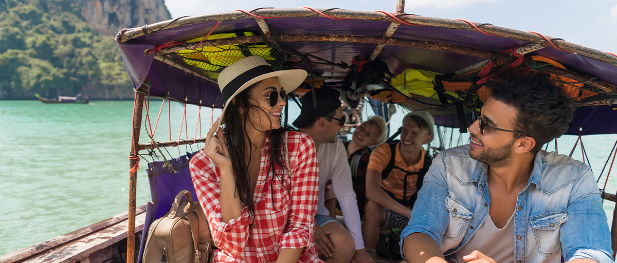 A group of friends look out over the waters while riding in a traditional boat in Thailand.