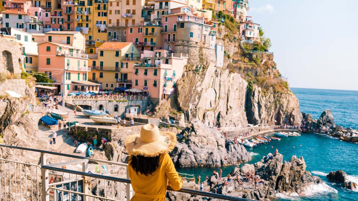 A woman in a yellow dress looks out on Manarola Village in Italy's Cinque Terre.